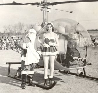 Santa and a woman elf next to a helicopter