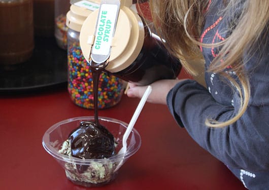 girl pouring chocolate on make your own sundae