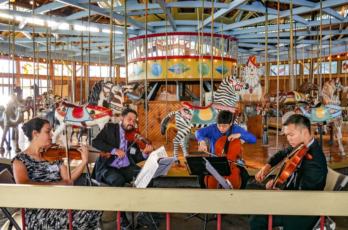 Violin Quartet in front of a carousel.
