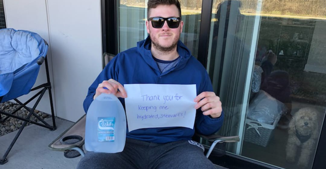 A man holding a gallon of water and a sign that reads thank you for keeping me hydrated, Stewarts.