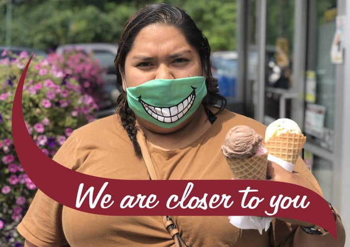 Woman holding two ice cream cones wearing a mask with a smile image. We are closer to you.