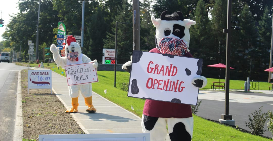 The Stewarts mascots Fresh the chicken and Flavor the Cow holding signs Eggcelent deals and Grand opening