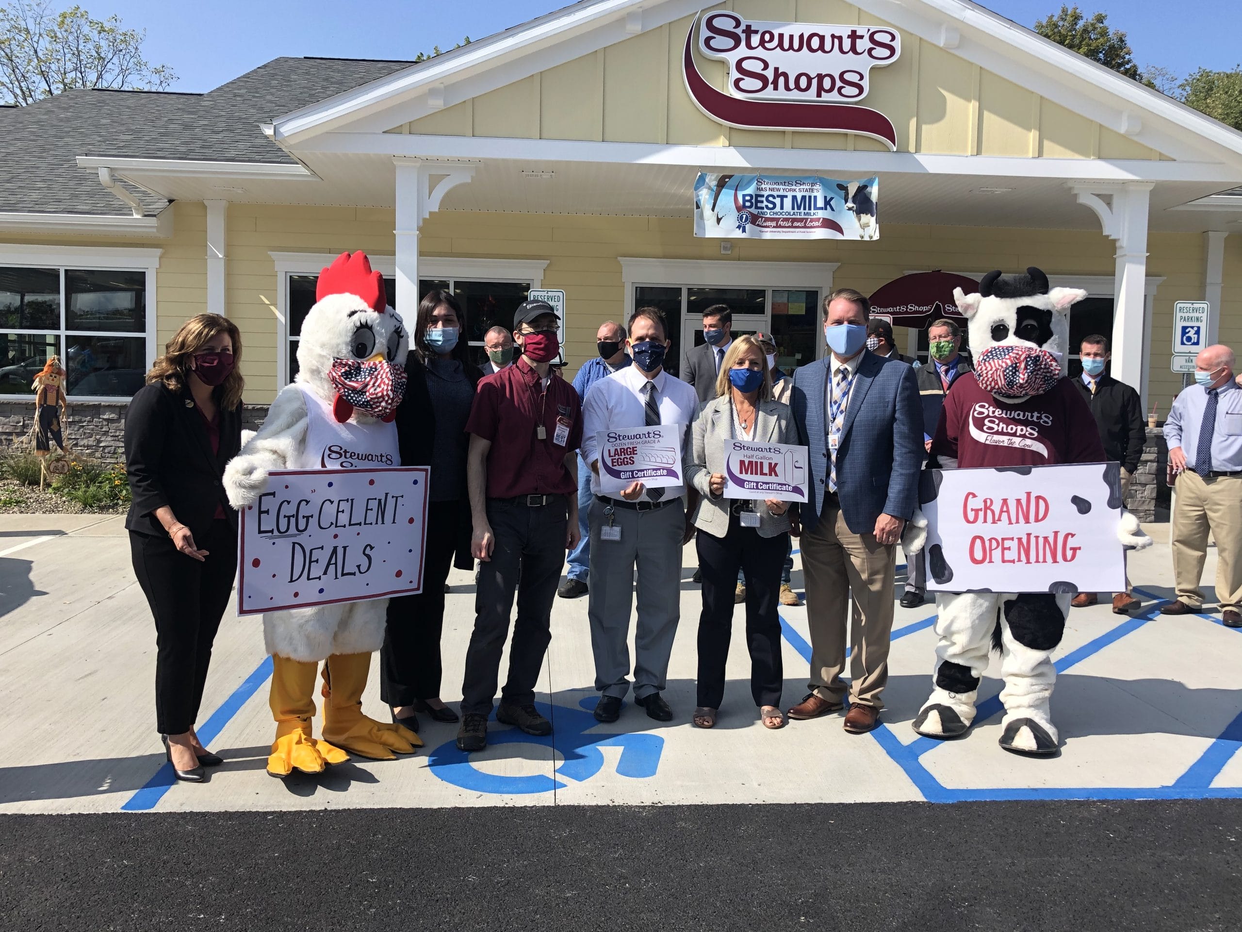 A group of people holding signs at a grand opening event at Stewarts. Eggcelent Deals, Large eggs, Milk, Grand Opening.