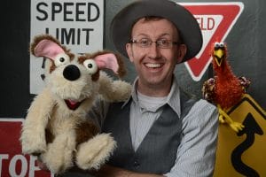 The Mesner Puppet Theater actor posing with a dog and chicken puppet.