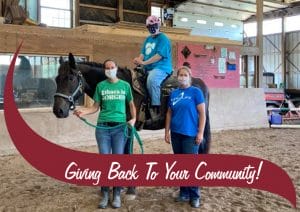 Two volunteers with an Athelas horseback rider, maroon waving that says "giving back to your community"
