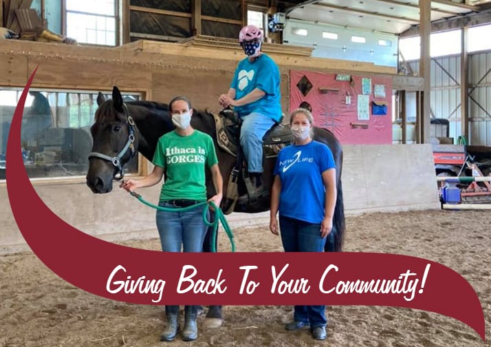 Two volunteers with an Athelas horseback rider, maroon waving that says "giving back to your community"