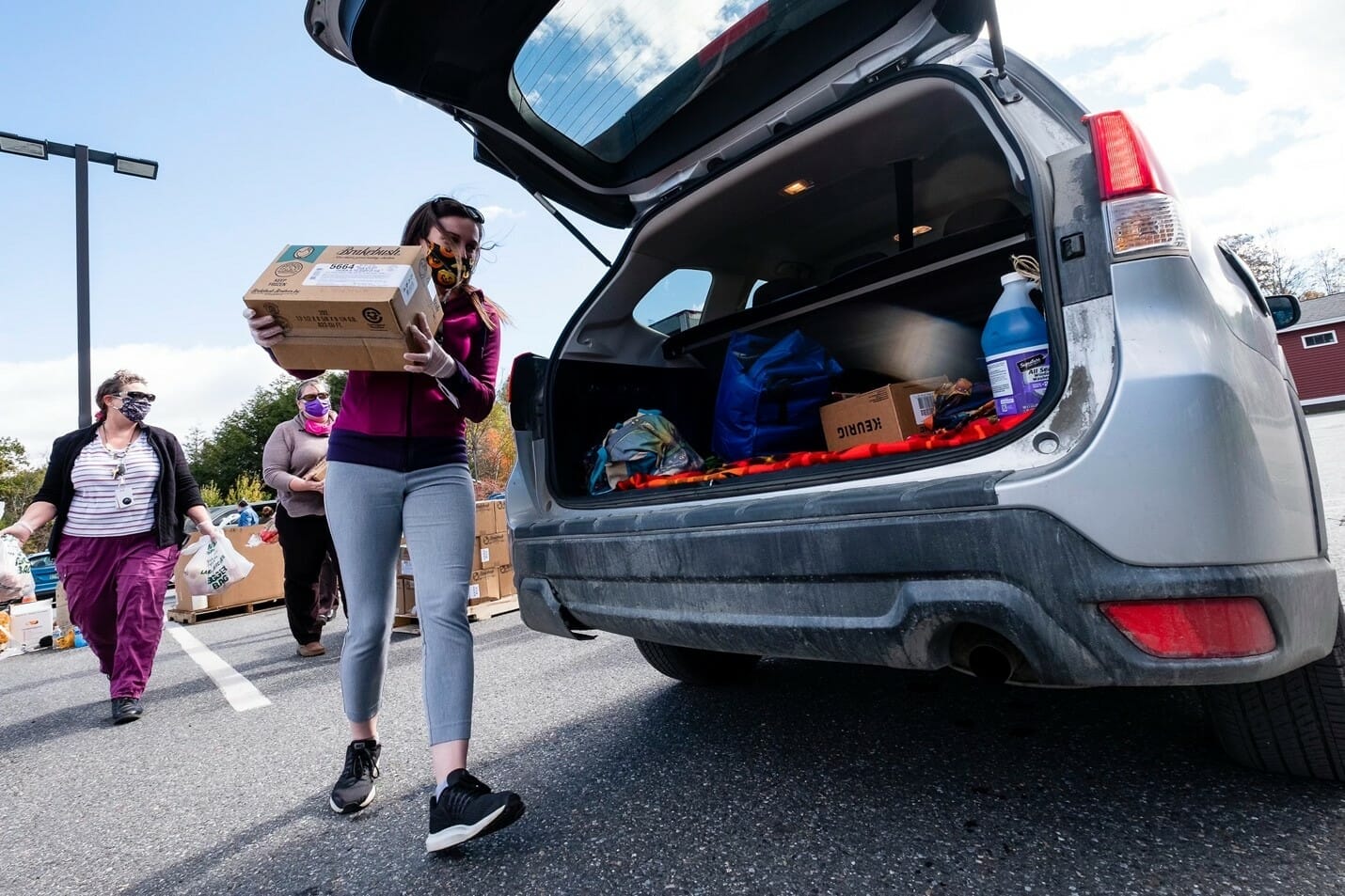a woman carrying a box of food to an open trunk of a car