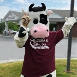Flavor the Cow holding a waffle cone in front of a Shop.