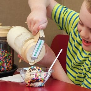 Kid pouring marshmallow sauce on a make your own sundae.