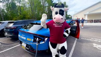 Flavor the cow waving in front of an electric vehicle 