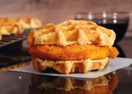 Spicy chicken between two waffles creating a sandwich.