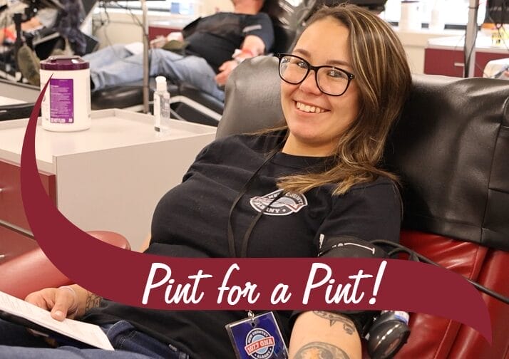 Woman giving blood with a maroon wave in front that reads, "Pint for a Pint".