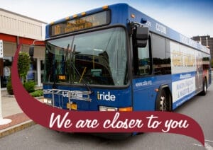 A blue CDTA bus with the route number 10 displayed on the front and the destination listed as 'Western Ave Downtown Albany' parked on a street. The side of the bus features an advertisement, and the front displays the CDTA and 'iride' logos. The background shows a sidewalk with trees and a building. A maroon banner with white text reading 'We are closer to you' overlays the bottom of the image.