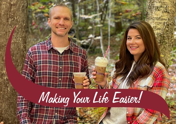 A man and woman standing outdoors in a wooded area, both wearing plaid shirts and holding Stewart's Shops iced coffee drinks with straws, paired with the text banner 'Making Your Life Easier!