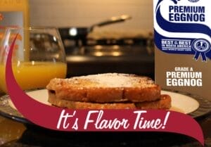 A plate of French toast dusted with powdered sugar sits on a kitchen countertop, accompanied by a glass of orange juice. In the background, a bottle of orange juice and a stovetop with a frying pan are visible. On the right side, a carton of Stewart's Premium Eggnog is partially visible, displaying a blue ribbon label that reads 'Best of the Best in North America 2023 World Dairy Expo.' A maroon banner with white text reading 'It's Flavor Time!' overlays the bottom of the image.