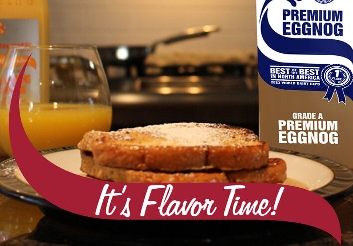 A plate of French toast dusted with powdered sugar sits on a kitchen countertop, accompanied by a glass of orange juice. In the background, a bottle of orange juice and a stovetop with a frying pan are visible. On the right side, a carton of Stewart's Premium Eggnog is partially visible, displaying a blue ribbon label that reads 'Best of the Best in North America 2023 World Dairy Expo.' A maroon banner with white text reading 'It's Flavor Time!' overlays the bottom of the image.
