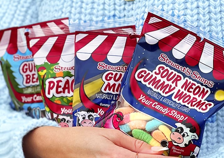 Person holding candy including Stewart's Sour Neon Gummy Worms, Peach Rings, Gummy Bears, and Gummy Mix-Up
